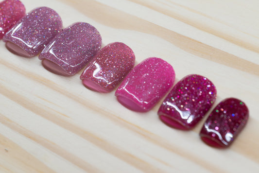 Pink glittery press on nails that range from dark to light across the fingers featured on a wooden background