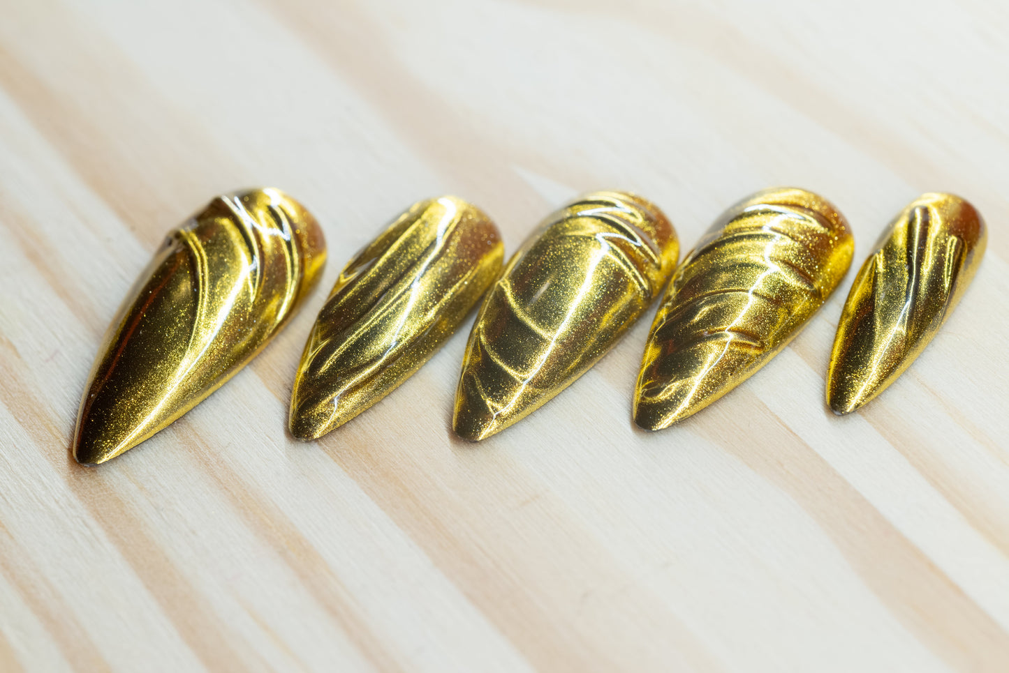 5 silver chrome and 5 gold chrome nails with abstract 3D swirls and lines featured on a wooden background