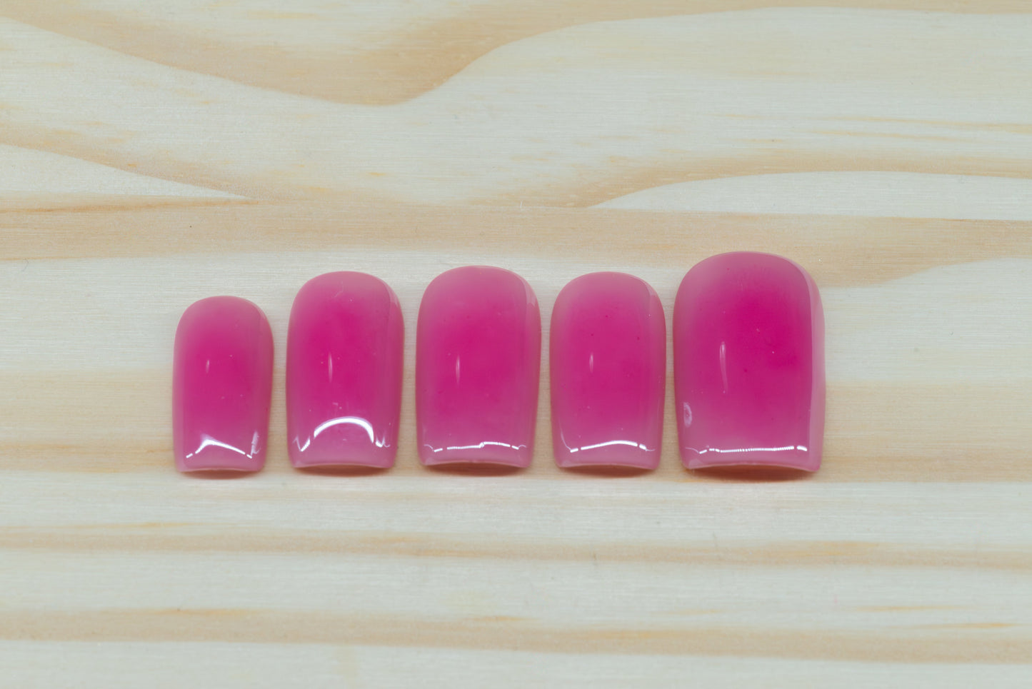 Berry pink aura-design press on nails featured on a wooden background
