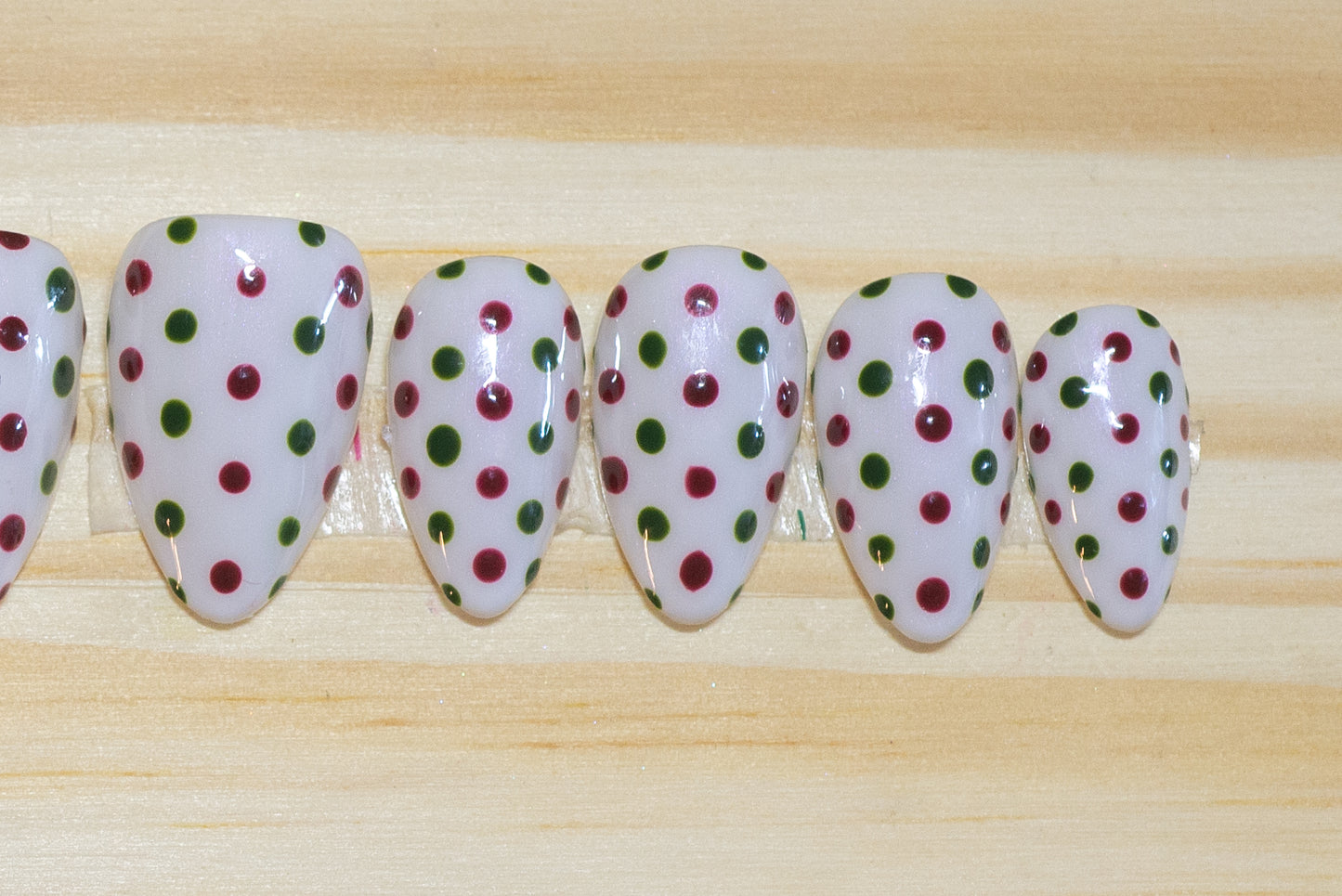 white press on nails with dark red and green polka dots on a wooden background