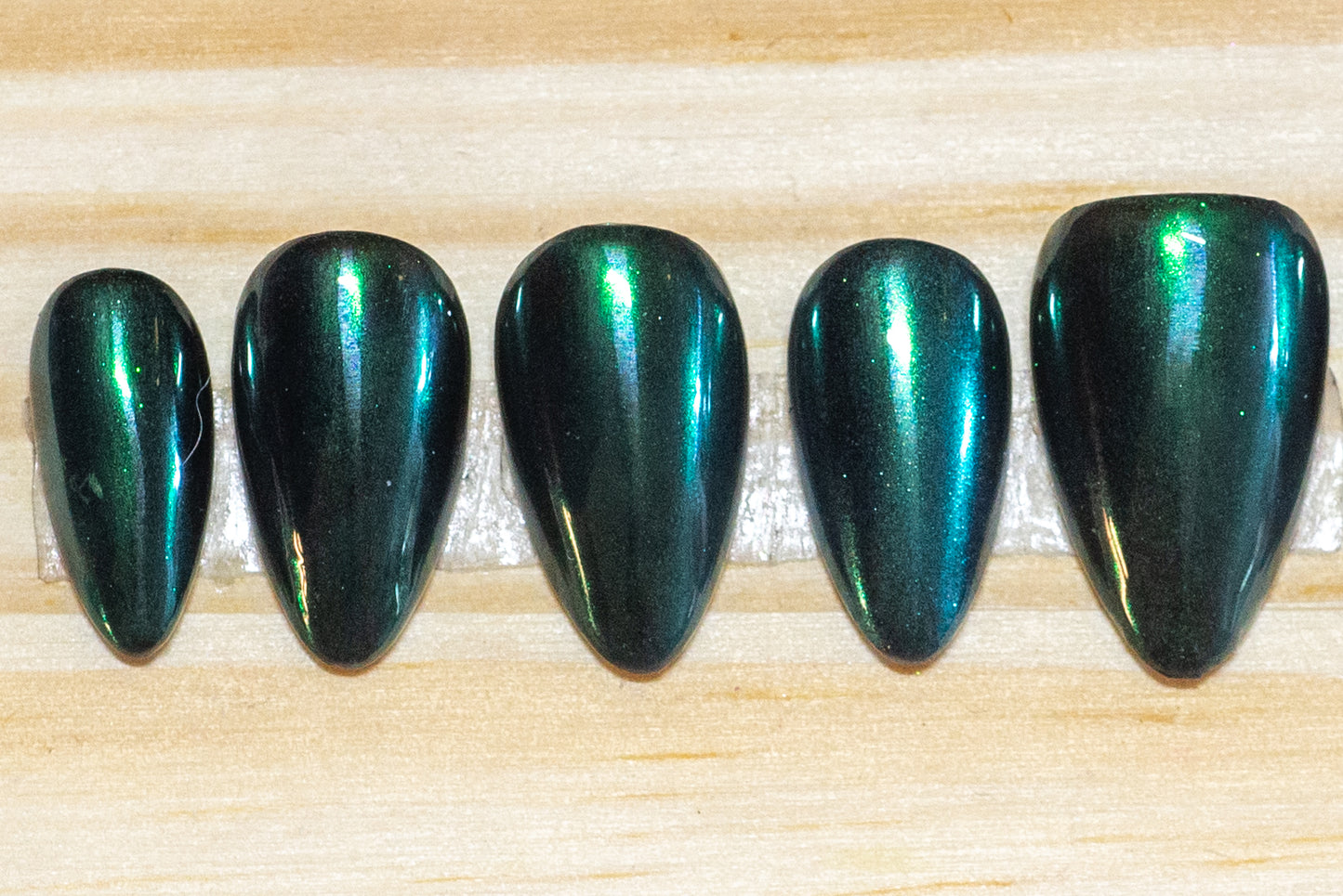 Metallic emerald green press on nails featured on a wooden background