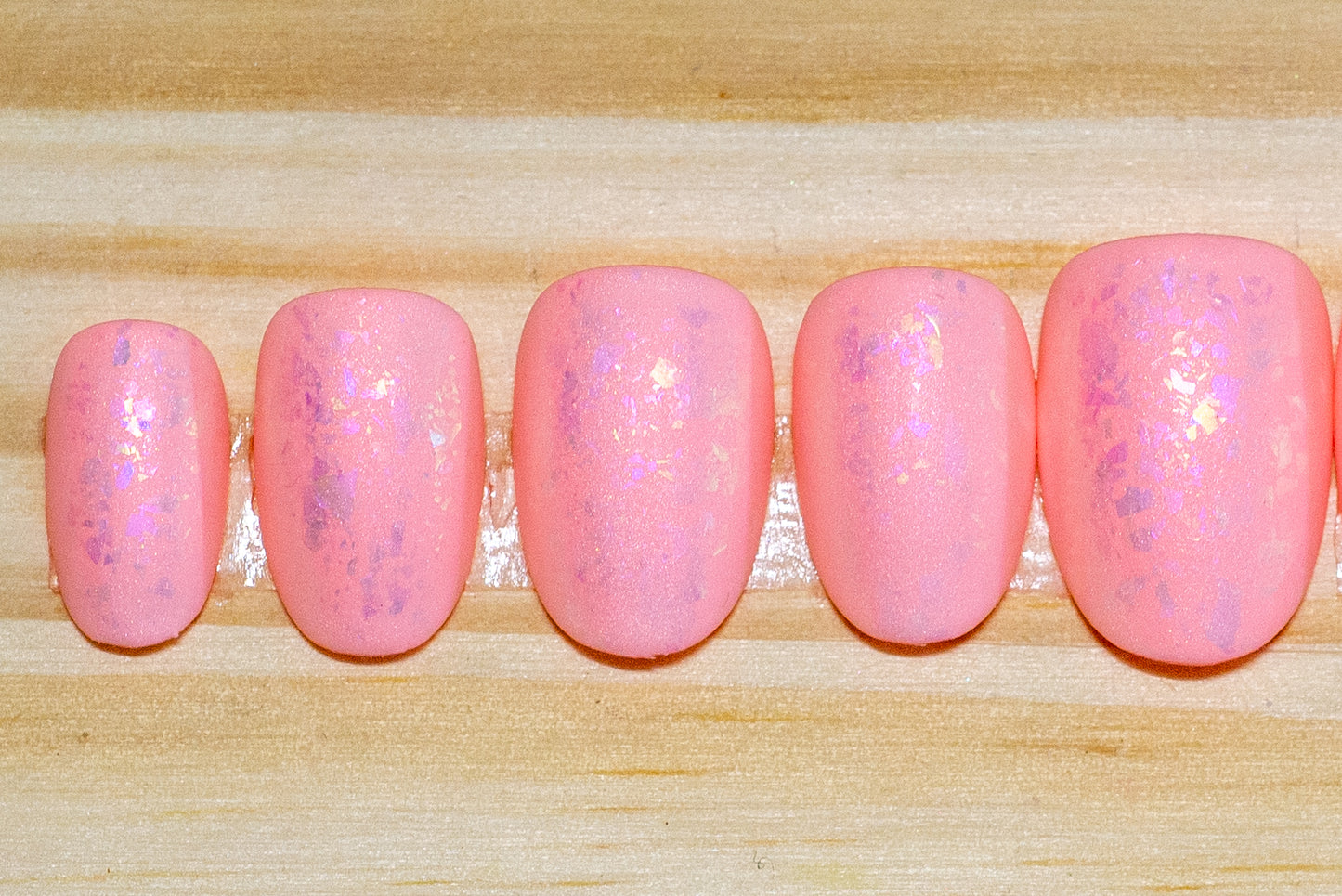 Peachy pink press on nails with pinky metallic flake and matte finish featured on a wooden background