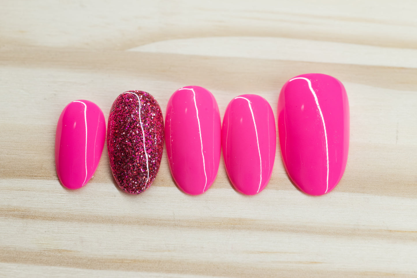 neon pink press on nails with one glitter nail each hand featured on a wooden background
