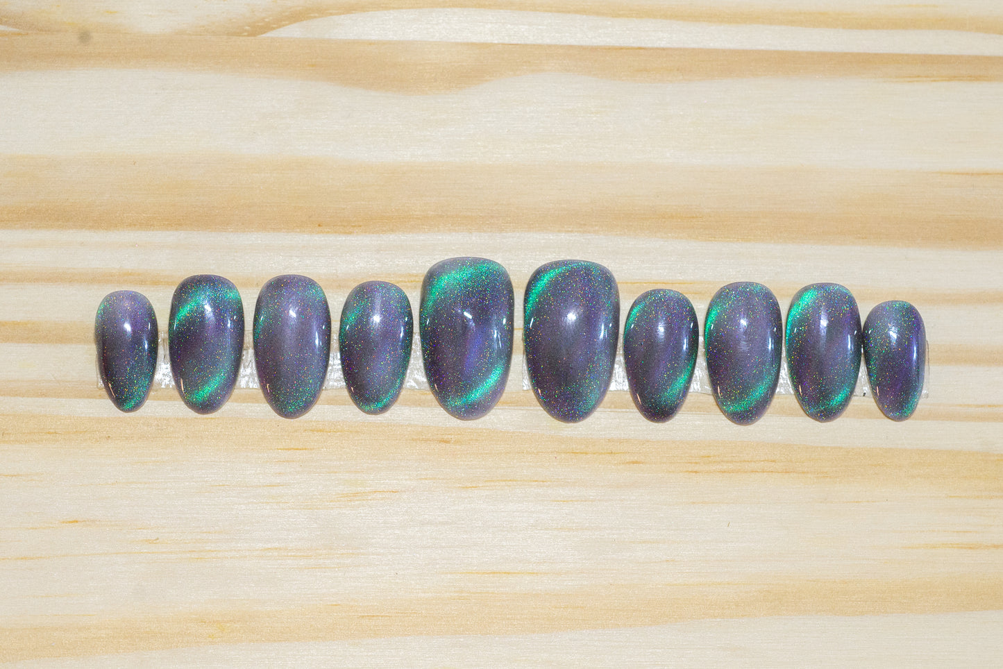 Press on nails with smoky sparkly grey base color and teal-purple cat eye flash featured on a wooden background