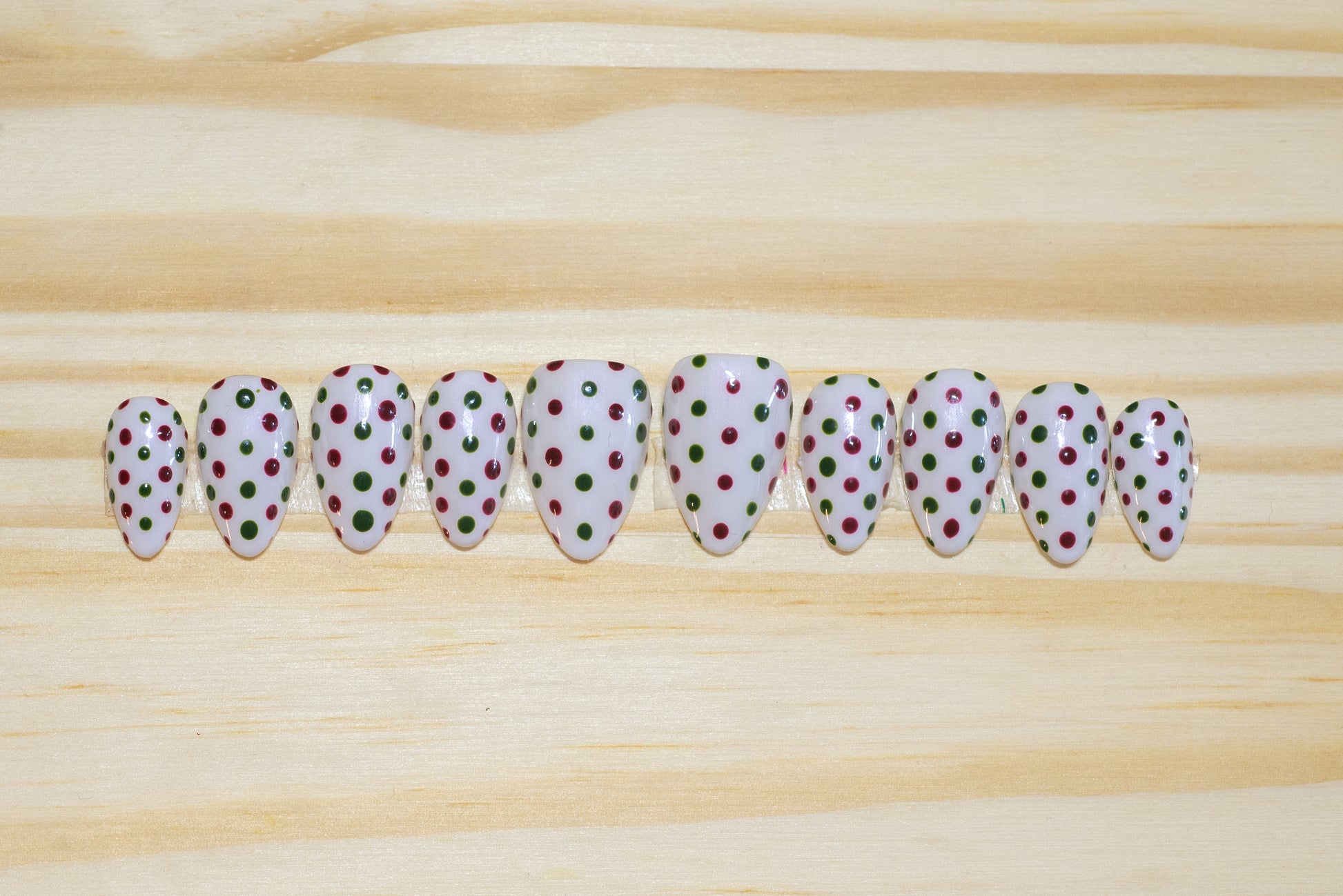 white press on nails with dark red and green polka dots on a wooden background