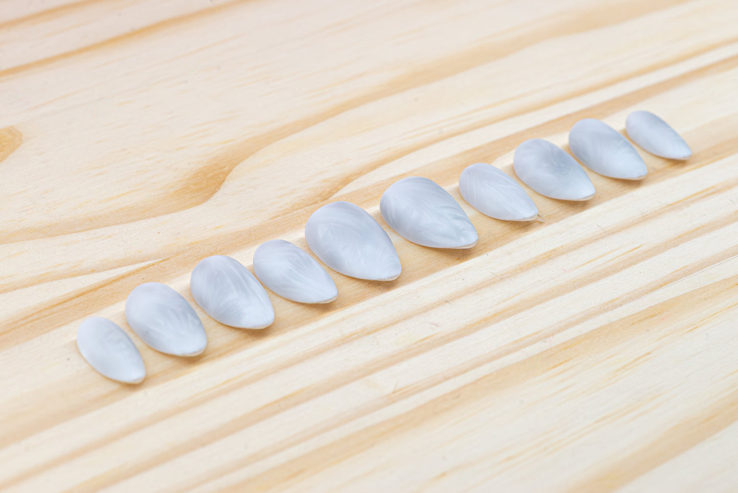 Icy white/silver cat eye press on nails that mimic the look of a frosty window, featured on a wooden background