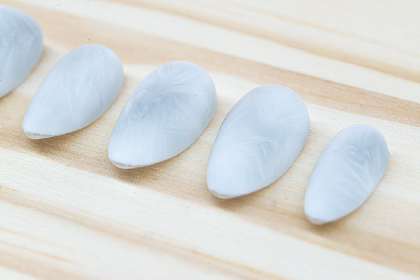 Icy white/silver cat eye press on nails that mimic the look of a frosty window, featured on a wooden background
