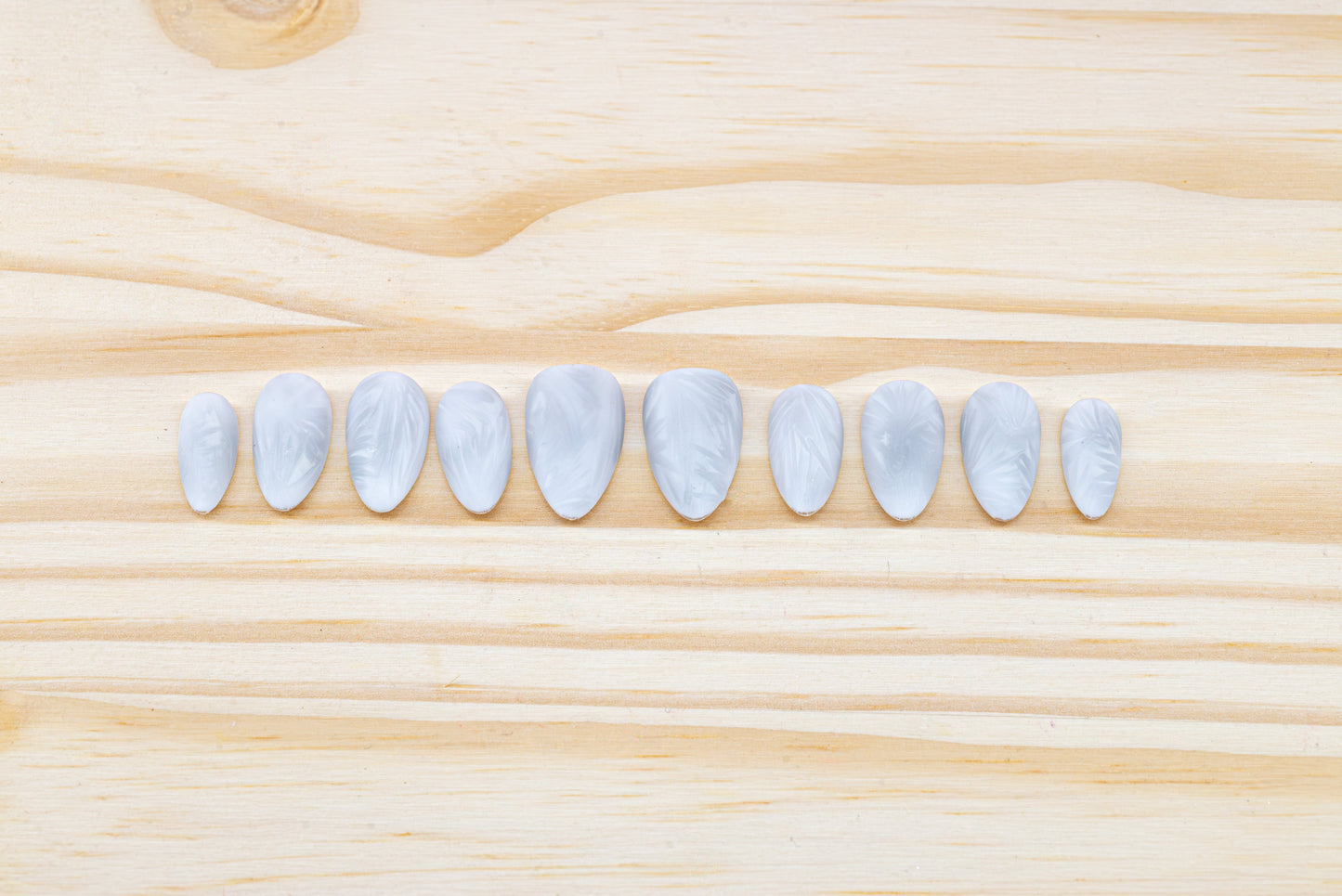 Icy white/silver cat eye press on nails that mimic the look of a frosty window, featured on a wooden background