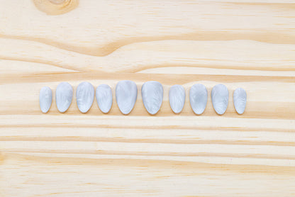 Icy white/silver cat eye press on nails that mimic the look of a frosty window, featured on a wooden background