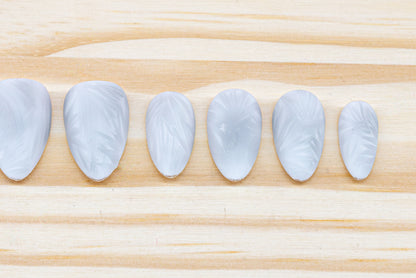 Icy white/silver cat eye press on nails that mimic the look of a frosty window, featured on a wooden background