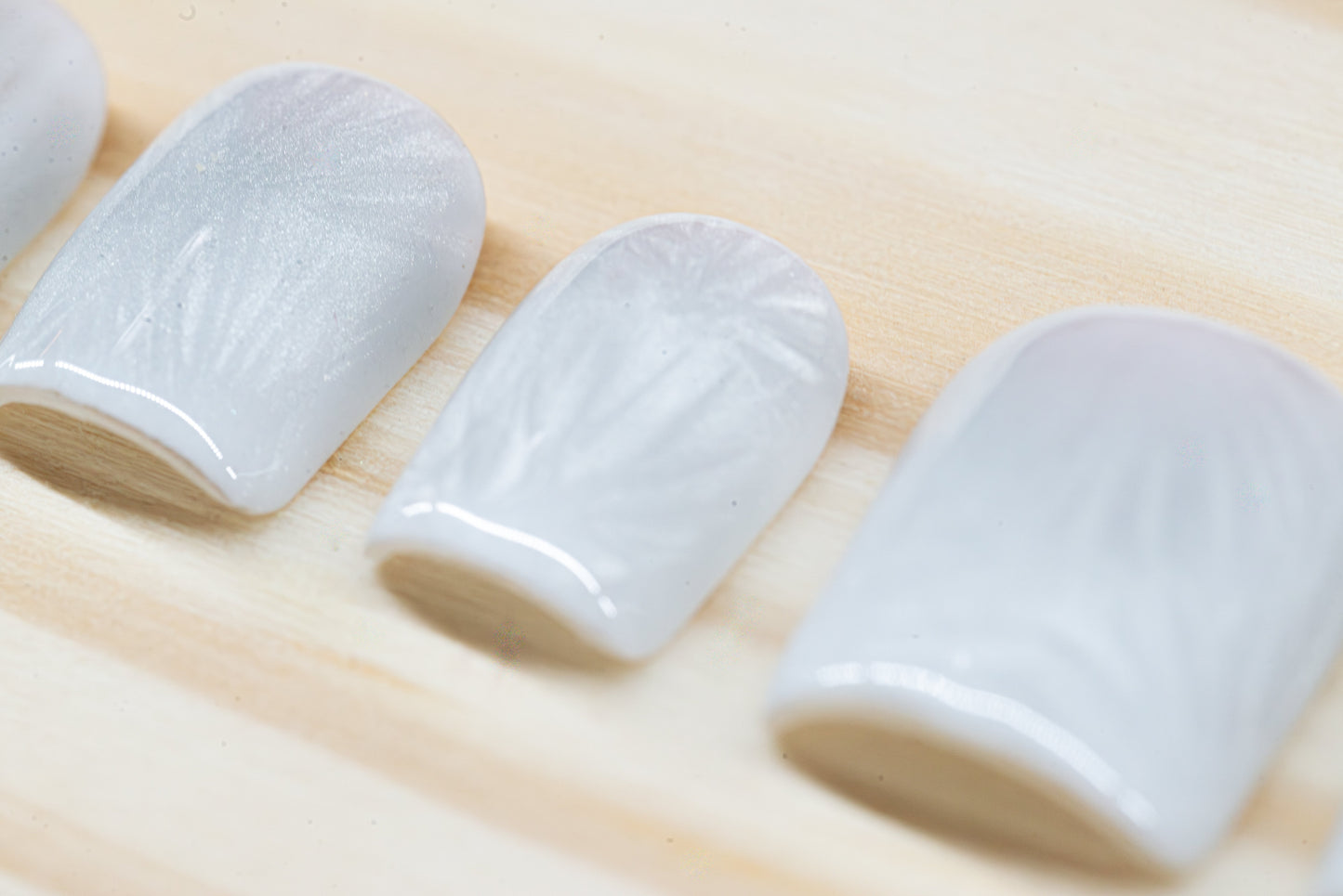 Icy white/silver cat eye press on nails that mimic the look of a frosty window, featured on a wooden background