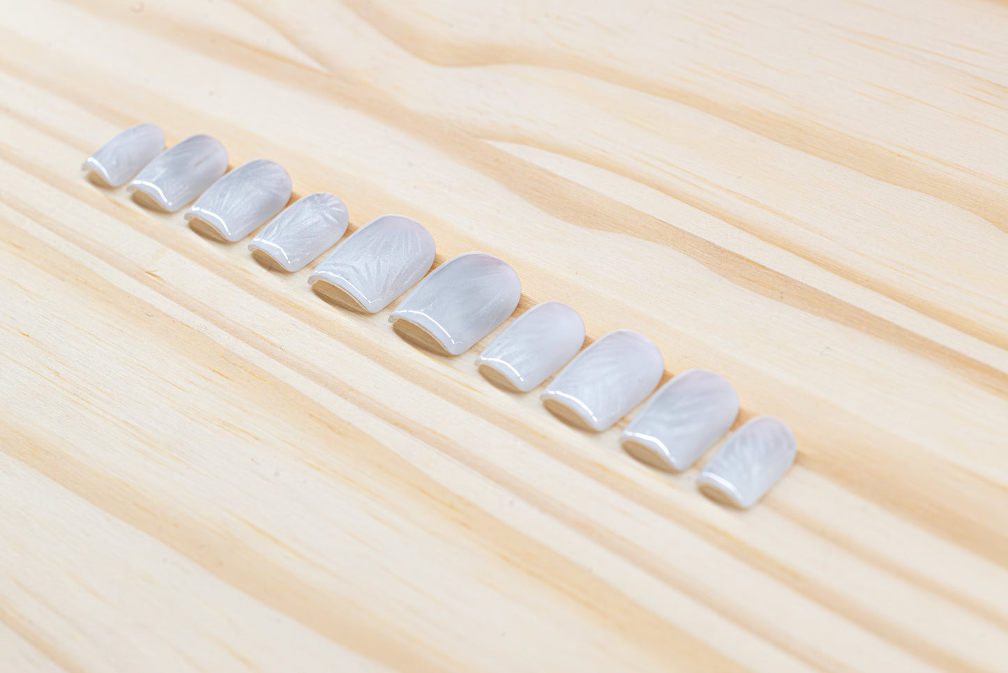 Icy white/silver cat eye press on nails that mimic the look of a frosty window, featured on a wooden background