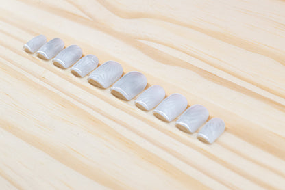 Icy white/silver cat eye press on nails that mimic the look of a frosty window, featured on a wooden background