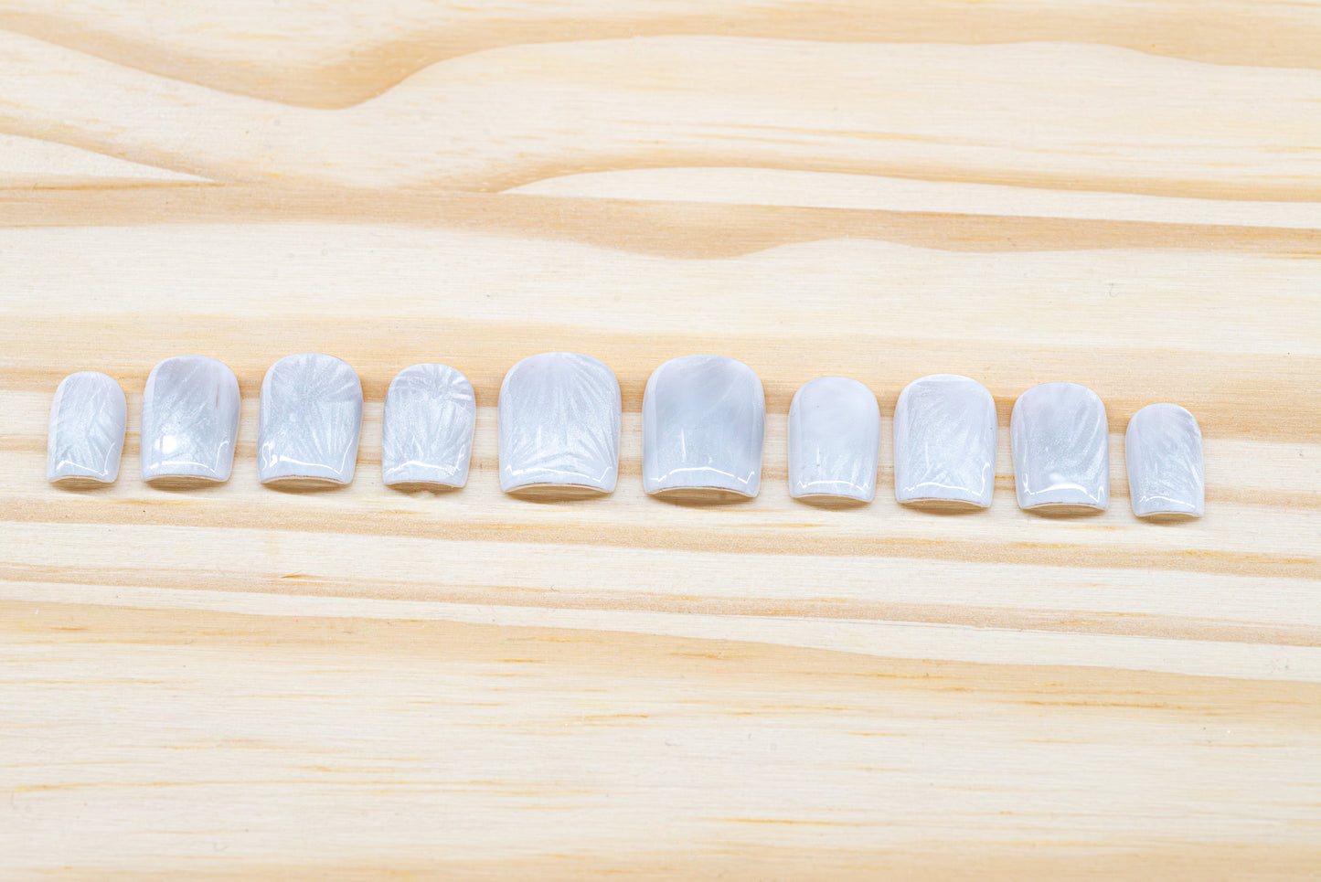 Icy white/silver cat eye press on nails that mimic the look of a frosty window, featured on a wooden background