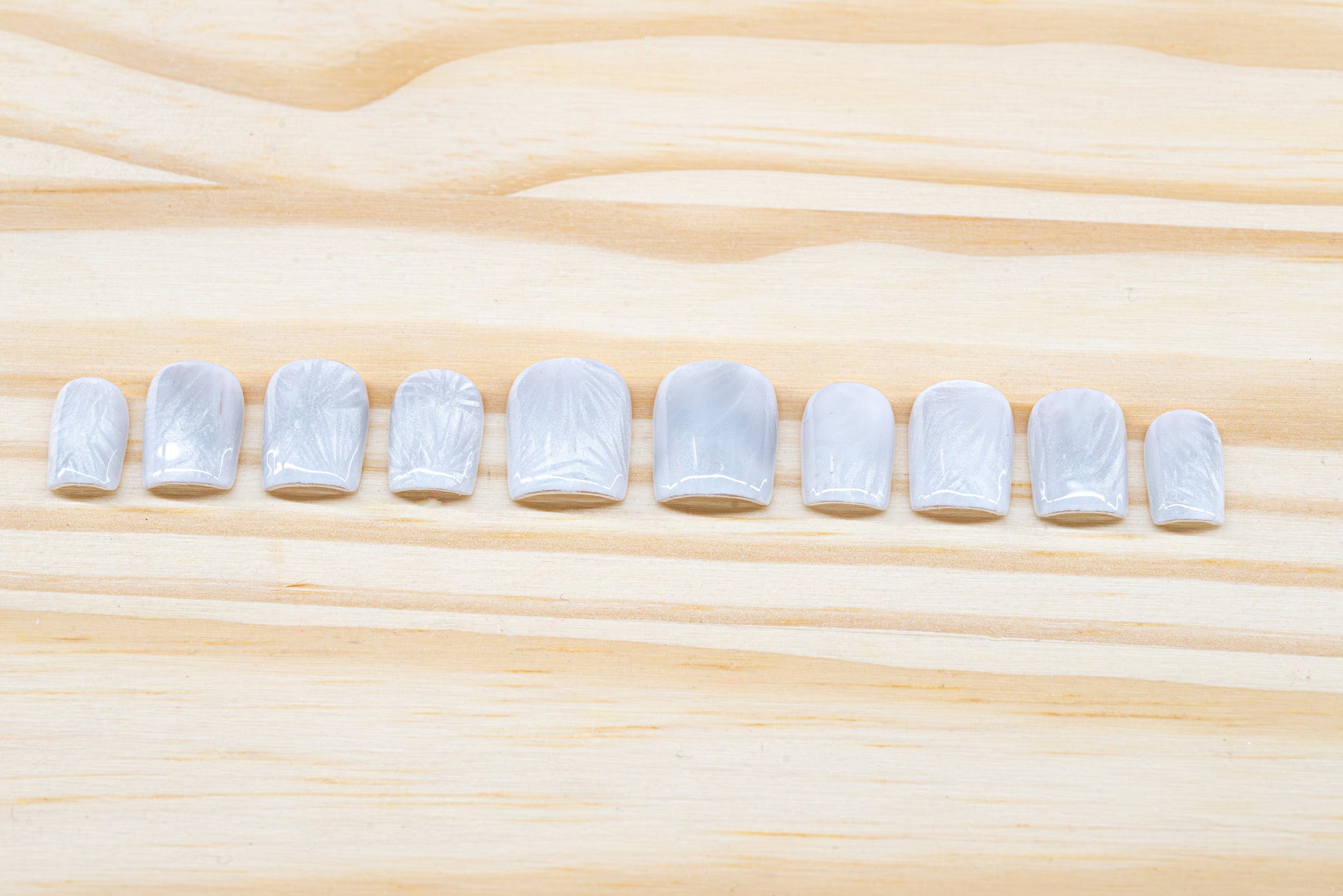 Icy white/silver cat eye press on nails that mimic the look of a frosty window, featured on a wooden background