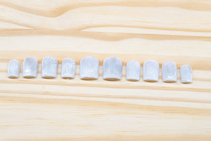 Icy white/silver cat eye press on nails that mimic the look of a frosty window, featured on a wooden background