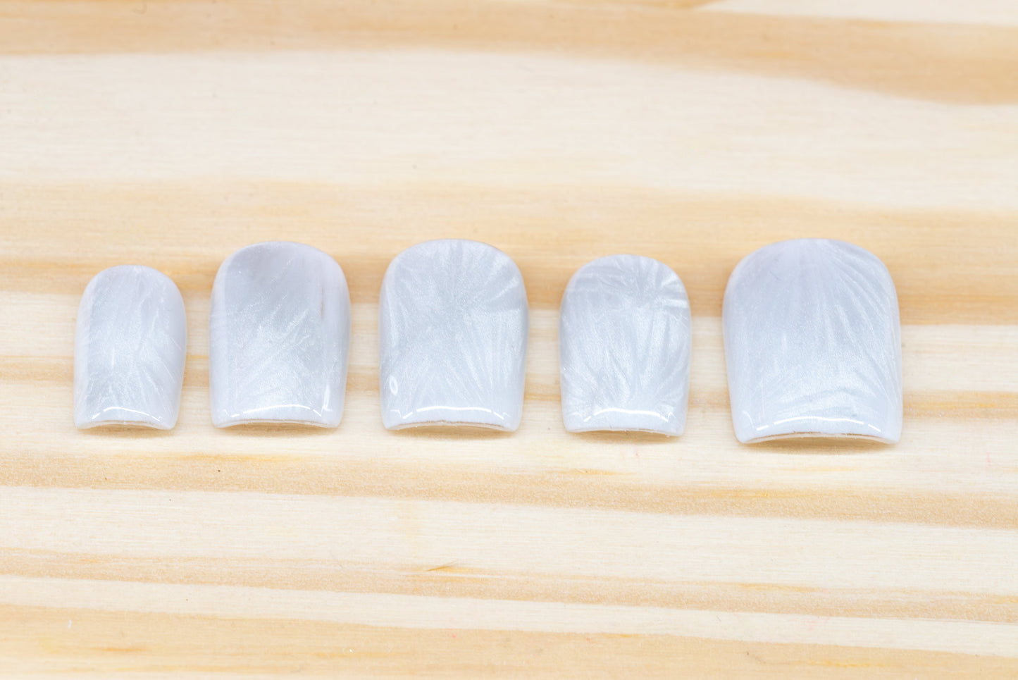 Icy white/silver cat eye press on nails that mimic the look of a frosty window, featured on a wooden background
