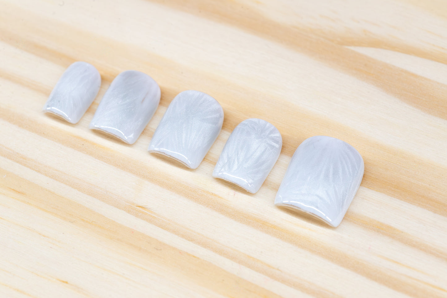 Icy white/silver cat eye press on nails that mimic the look of a frosty window, featured on a wooden background