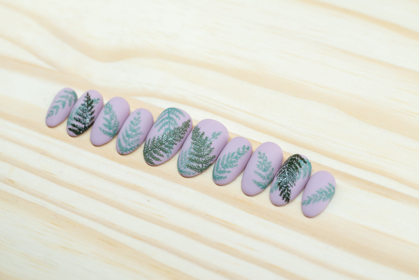 Mauve press on nails with fern motif featured on a wooden background