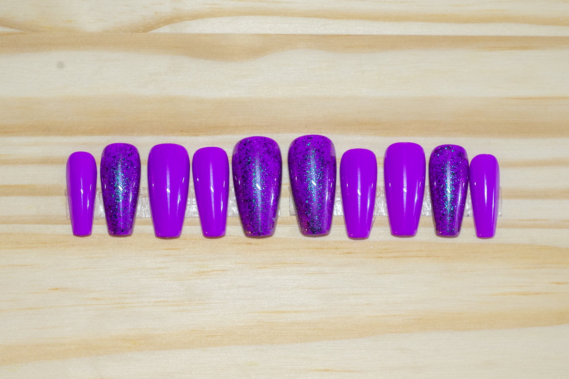 purple press on nails with purple glitter accent nails featured on a wooden background