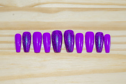 purple press on nails with purple glitter accent nails featured on a wooden background