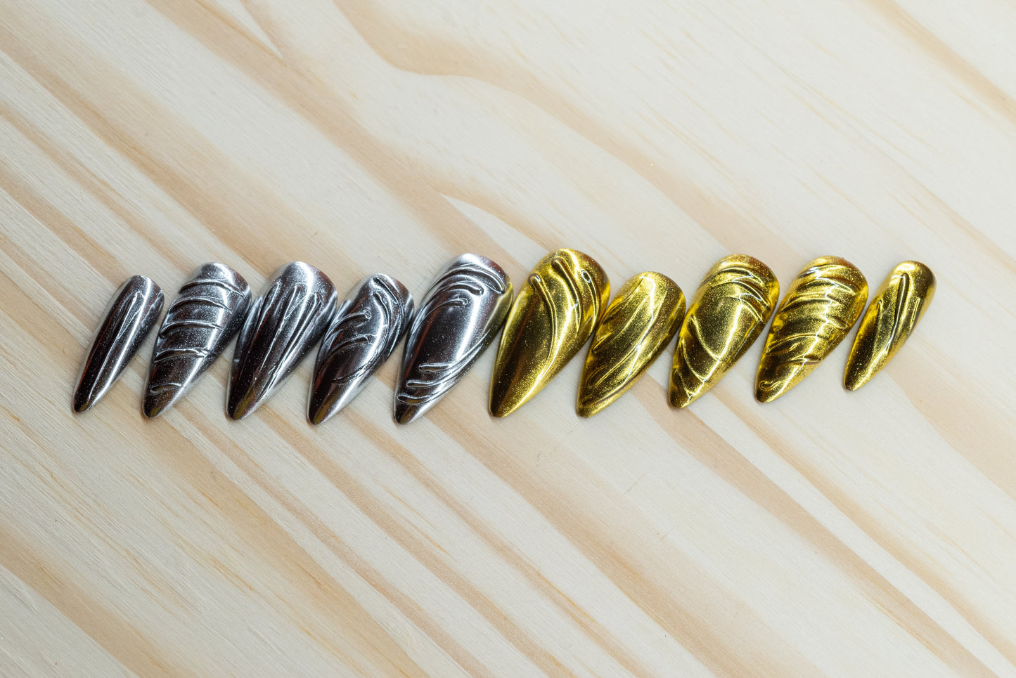 5 silver chrome and 5 gold chrome nails with abstract 3D swirls and lines featured on a wooden background
