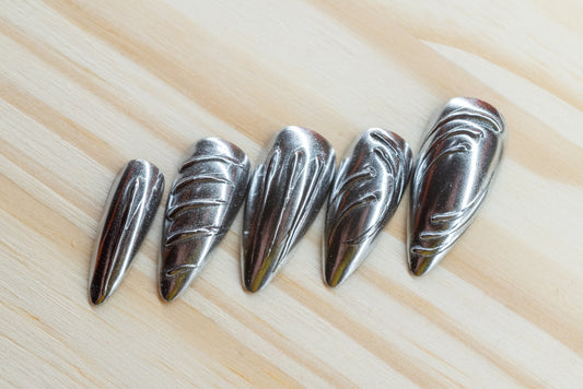 5 silver chrome and 5 gold chrome nails with abstract 3D swirls and lines featured on a wooden background
