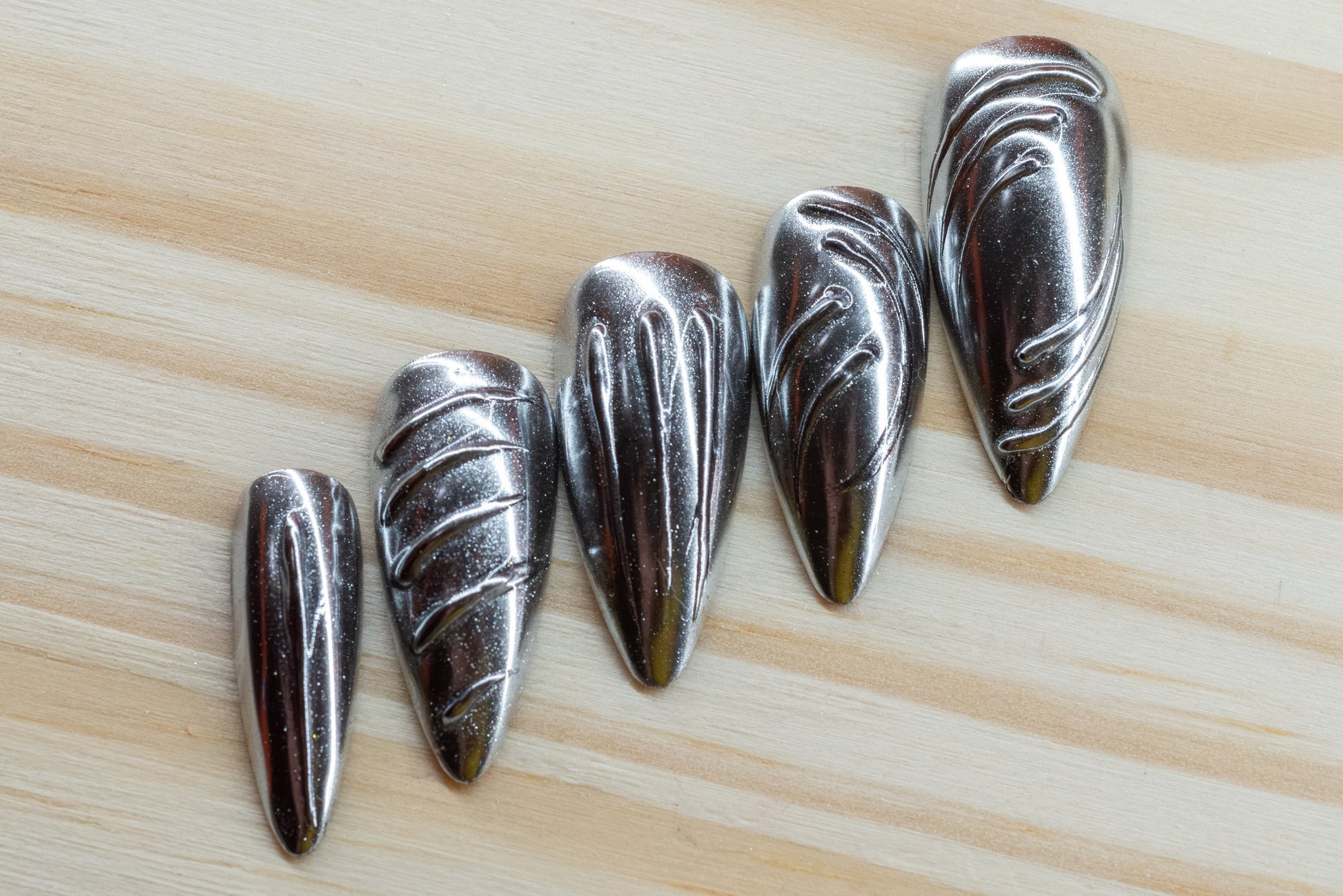 5 silver chrome and 5 gold chrome nails with abstract 3D swirls and lines featured on a wooden background
