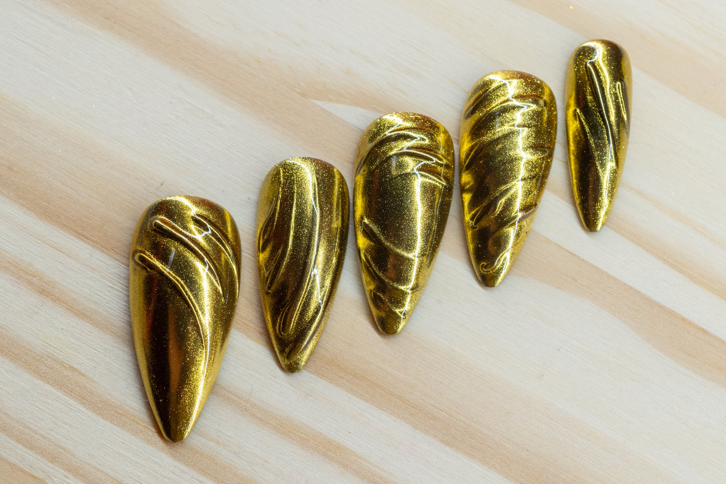 5 silver chrome and 5 gold chrome nails with abstract 3D swirls and lines featured on a wooden background