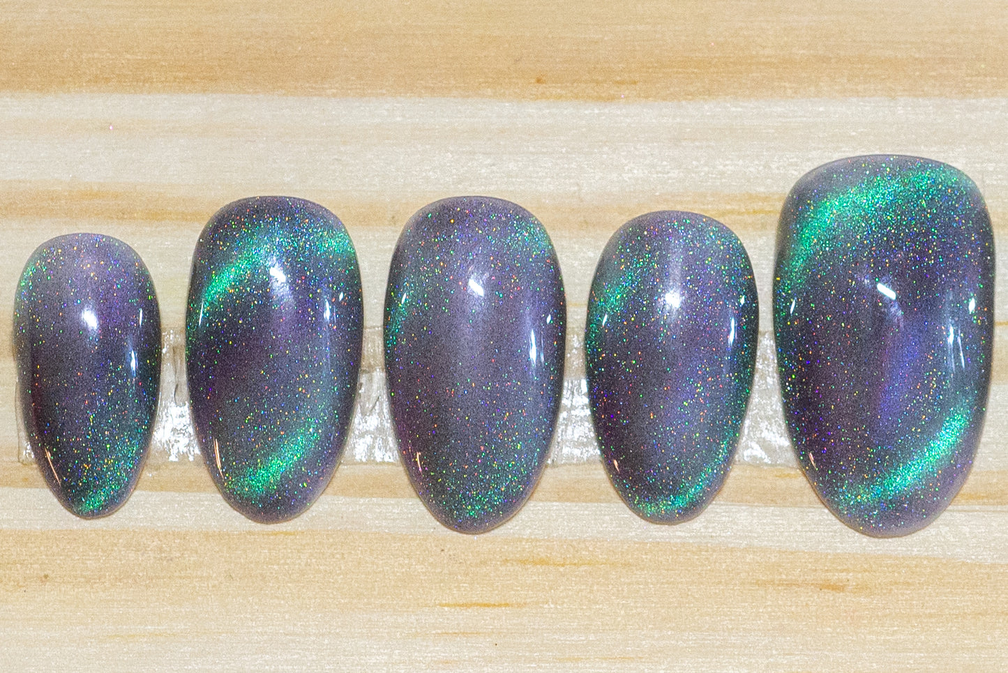 Press on nails with smoky sparkly grey base color and teal-purple cat eye flash featured on a wooden background