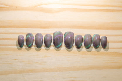 Press on nails with smoky sparkly grey base color and teal-purple cat eye flash featured on a wooden background