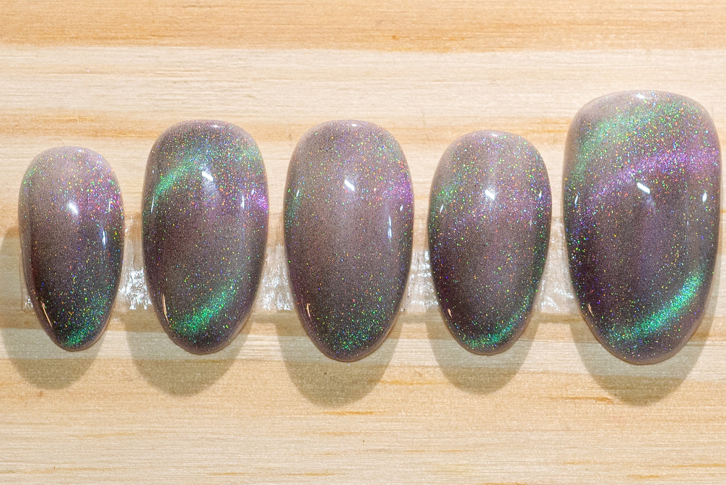 Press on nails with smoky sparkly grey base color and teal-purple cat eye flash featured on a wooden background