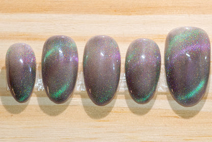 Press on nails with smoky sparkly grey base color and teal-purple cat eye flash featured on a wooden background