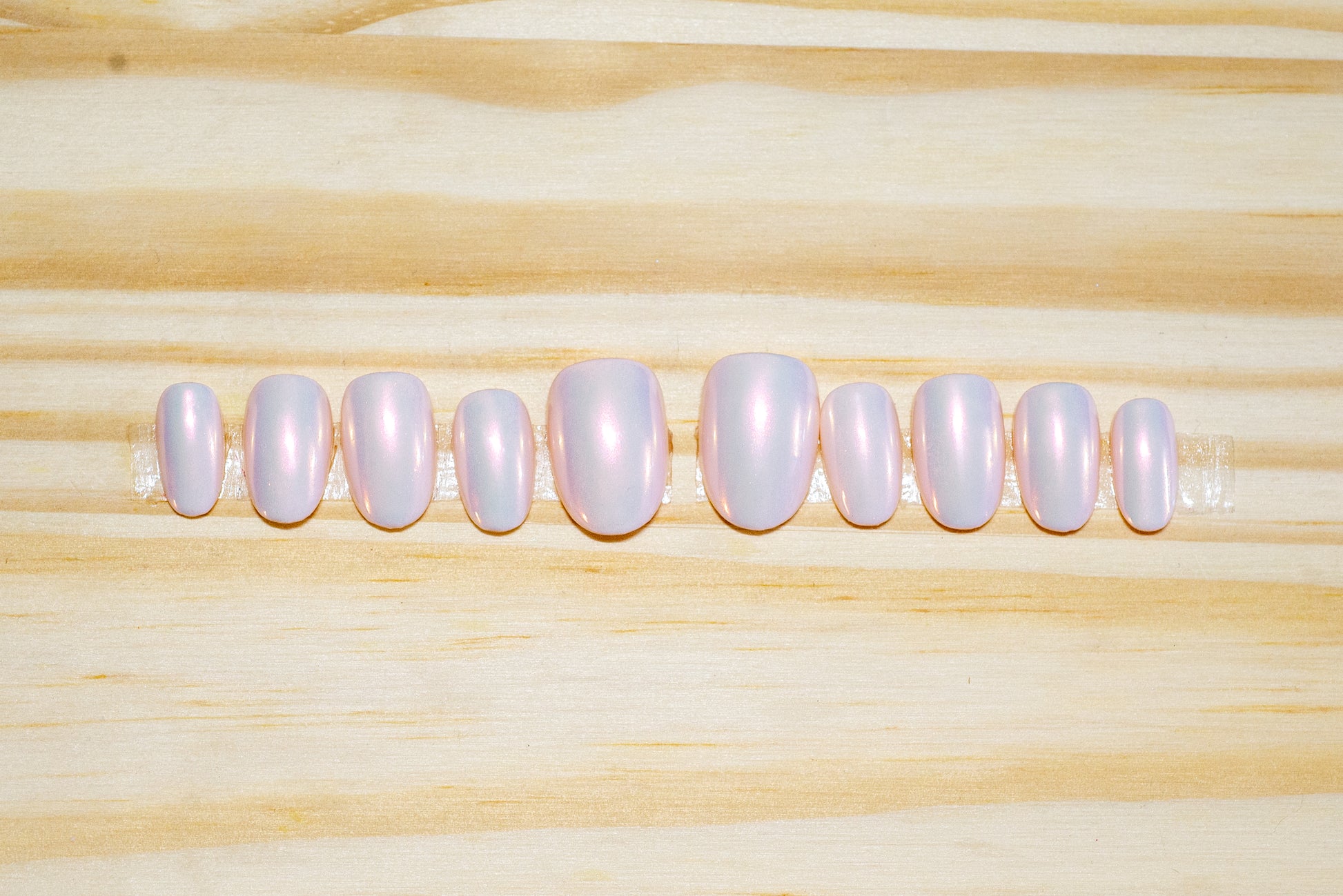 Pale pink press on nails with translucent pink/orange chrome glossy finish featured on a wooden background