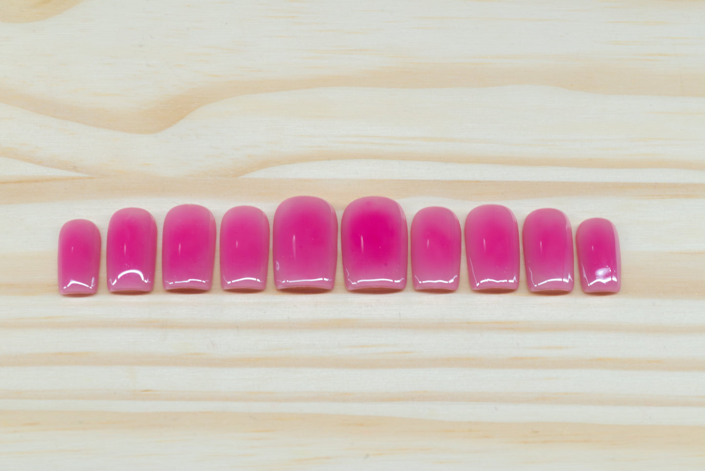 Berry pink aura-design press on nails featured on a wooden background