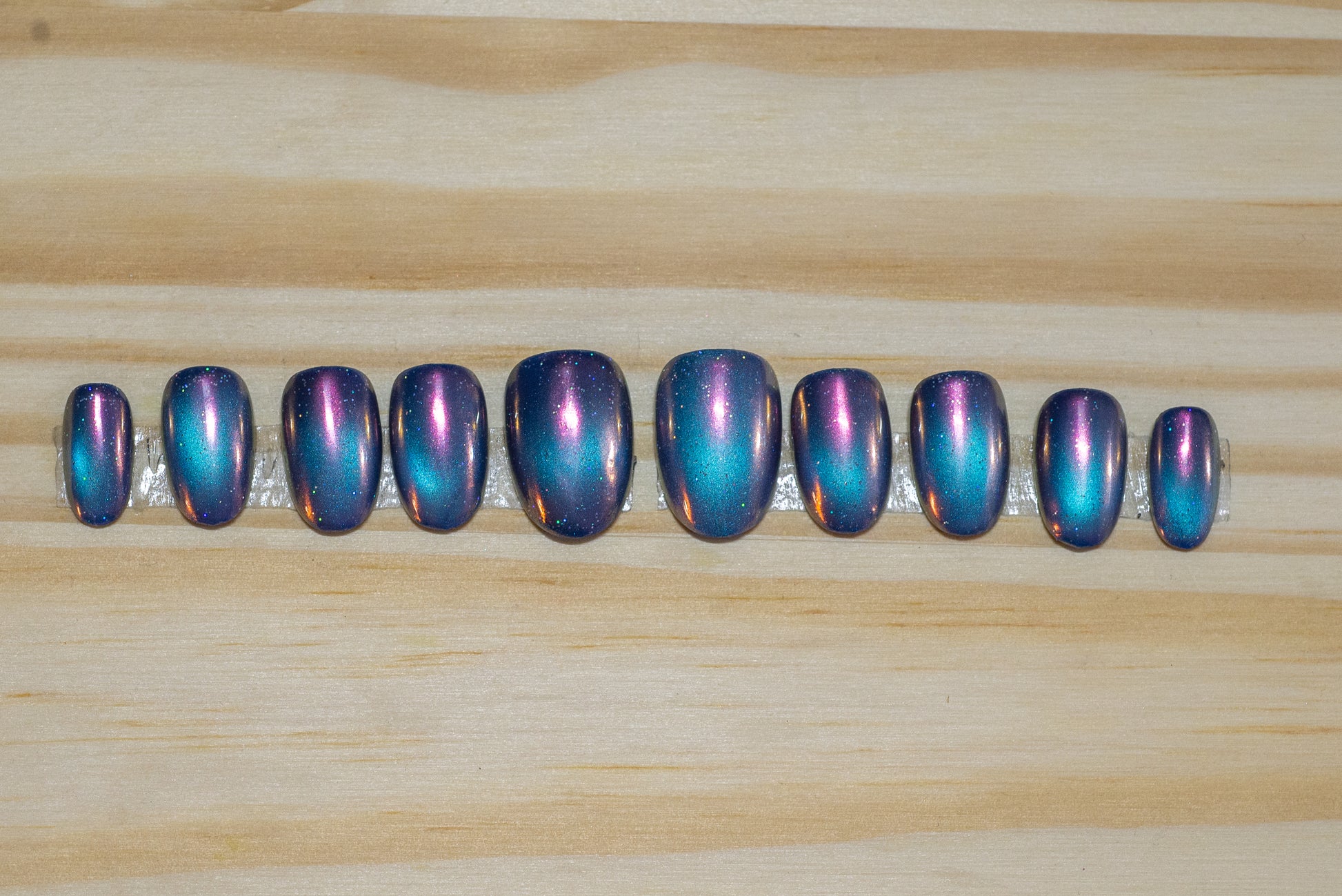 blue galaxy cateye with pink chrome overlay press on nails on a wooden background