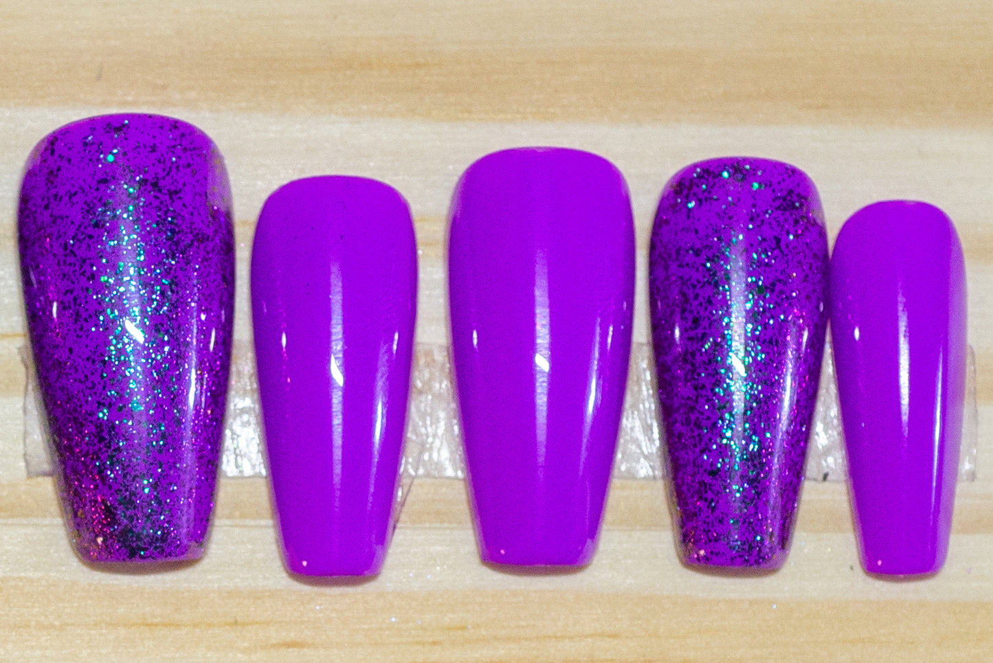 purple press on nails with purple glitter accent nails featured on a wooden background