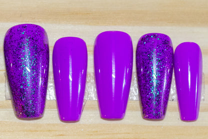 purple press on nails with purple glitter accent nails featured on a wooden background