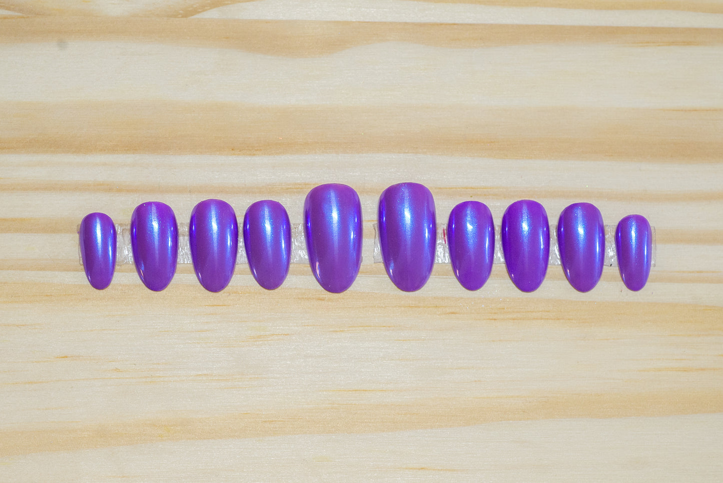 Purple press on nails with transparent blue chrome overlay featured on a wooden background