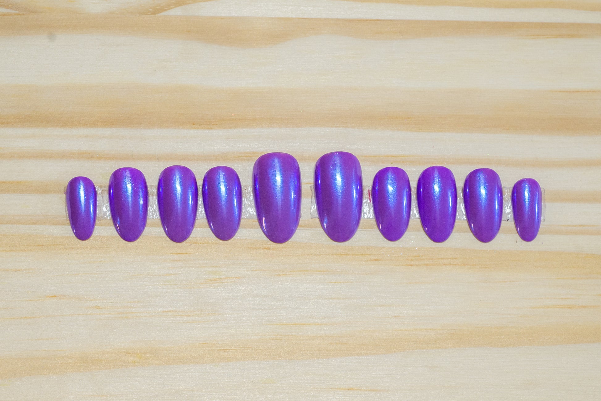 Purple press on nails with transparent blue chrome overlay featured on a wooden background