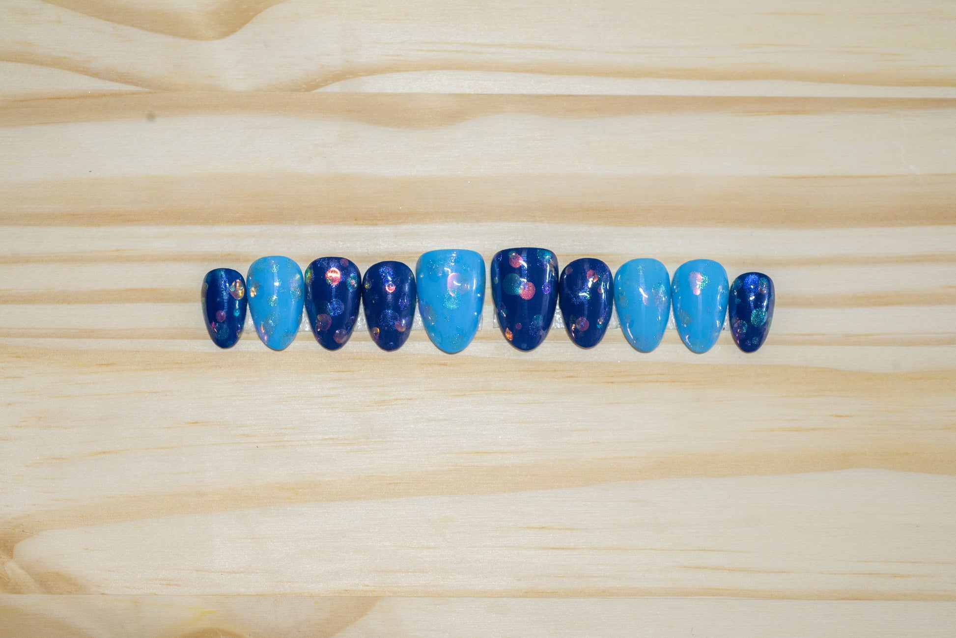 Light blue and dark blue press on nails with abstract bubble pattern featured on a wooden background