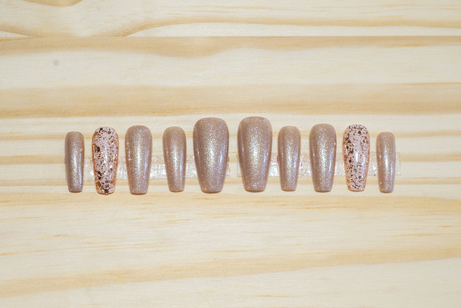 Shimmery champagne gold press on nails with glittery gold accent nails featured on a wooden background