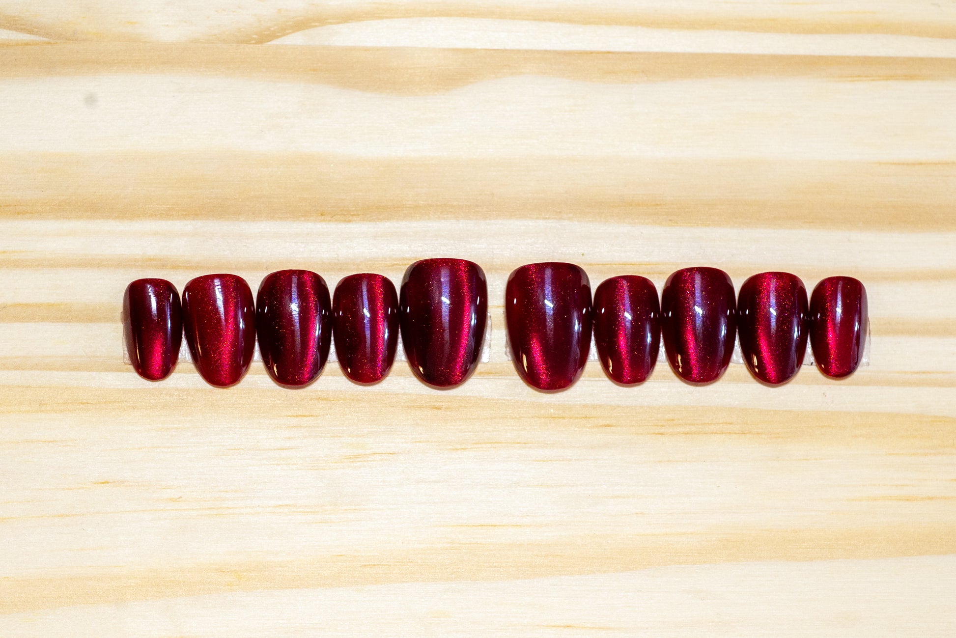 Dark cherry red cat eye effect press on nails featured on a wooden background