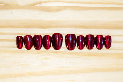 Dark cherry red cat eye effect press on nails featured on a wooden background