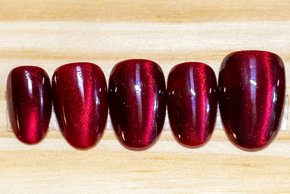 Dark cherry red cat eye effect press on nails featured on a wooden background