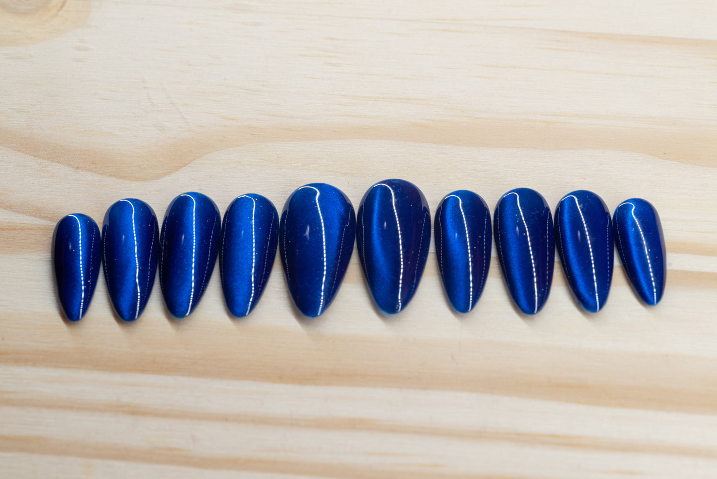 Deep blue cat eye effect press on nails featured on a wooden background