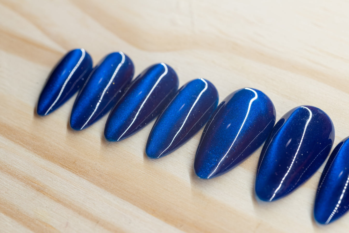 Deep blue cat eye effect press on nails featured on a wooden background