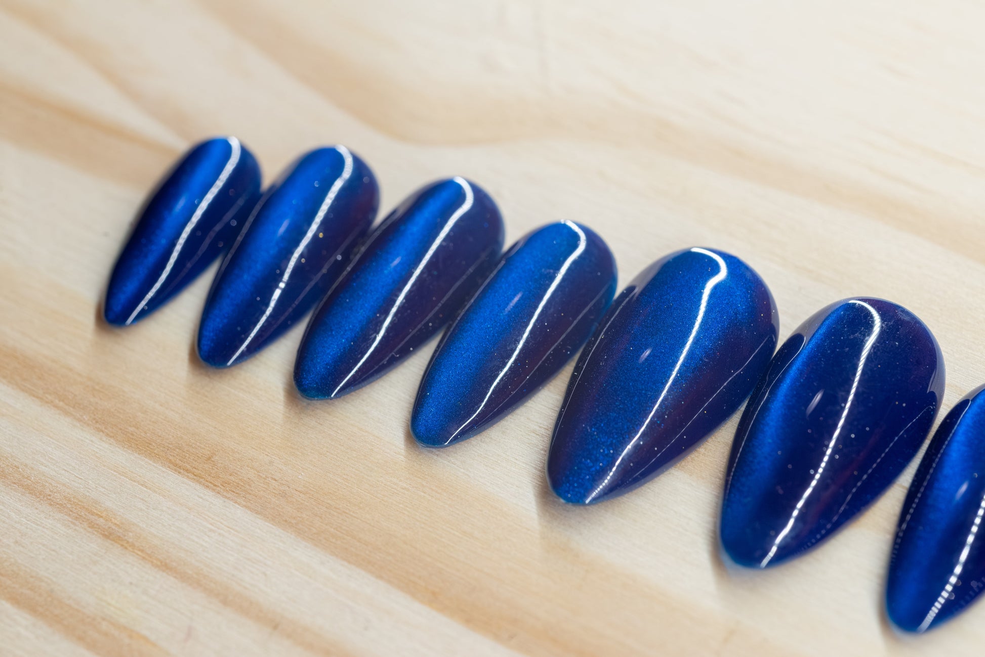 Deep blue cat eye effect press on nails featured on a wooden background