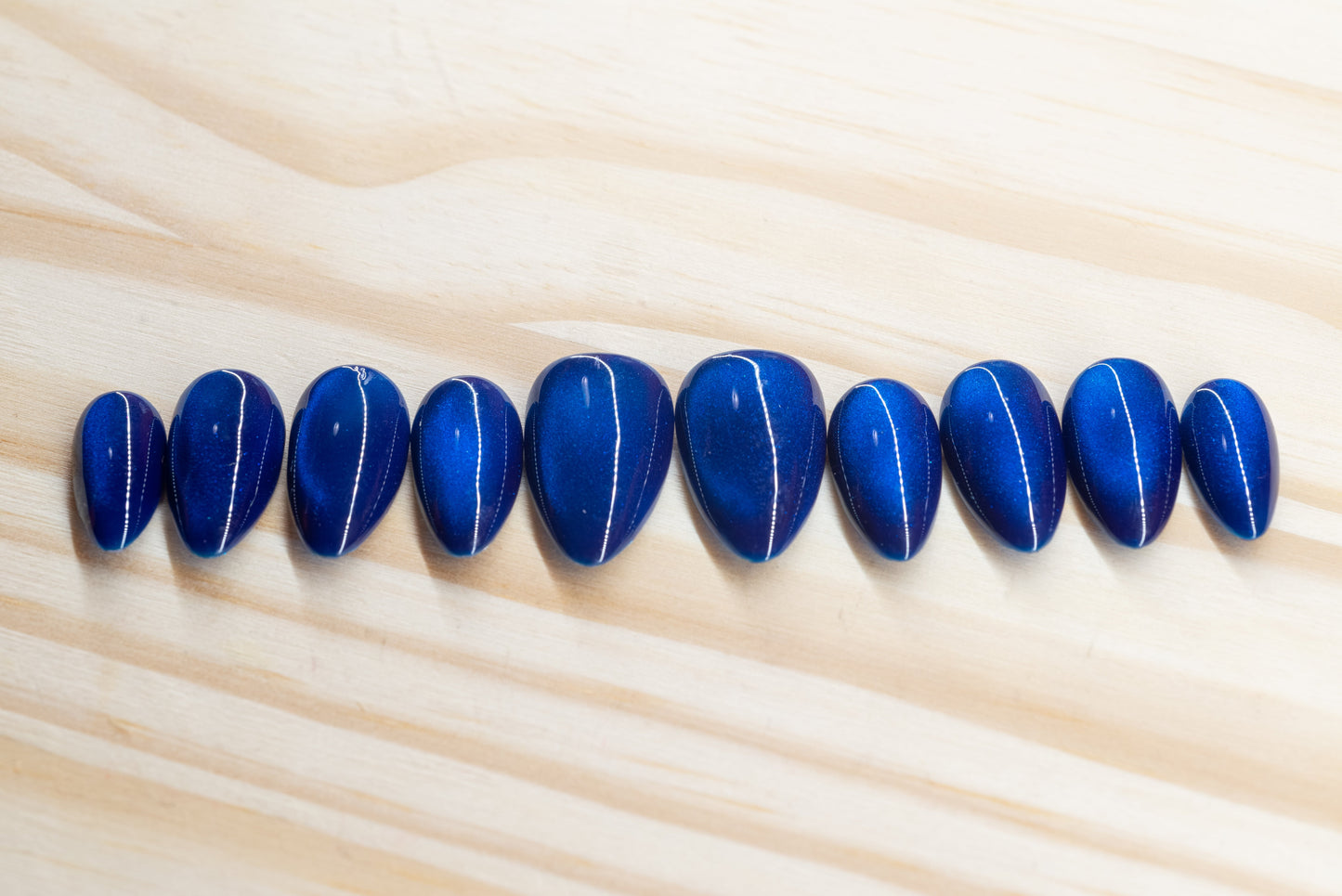 Deep blue cat eye effect press on nails featured on a wooden background
