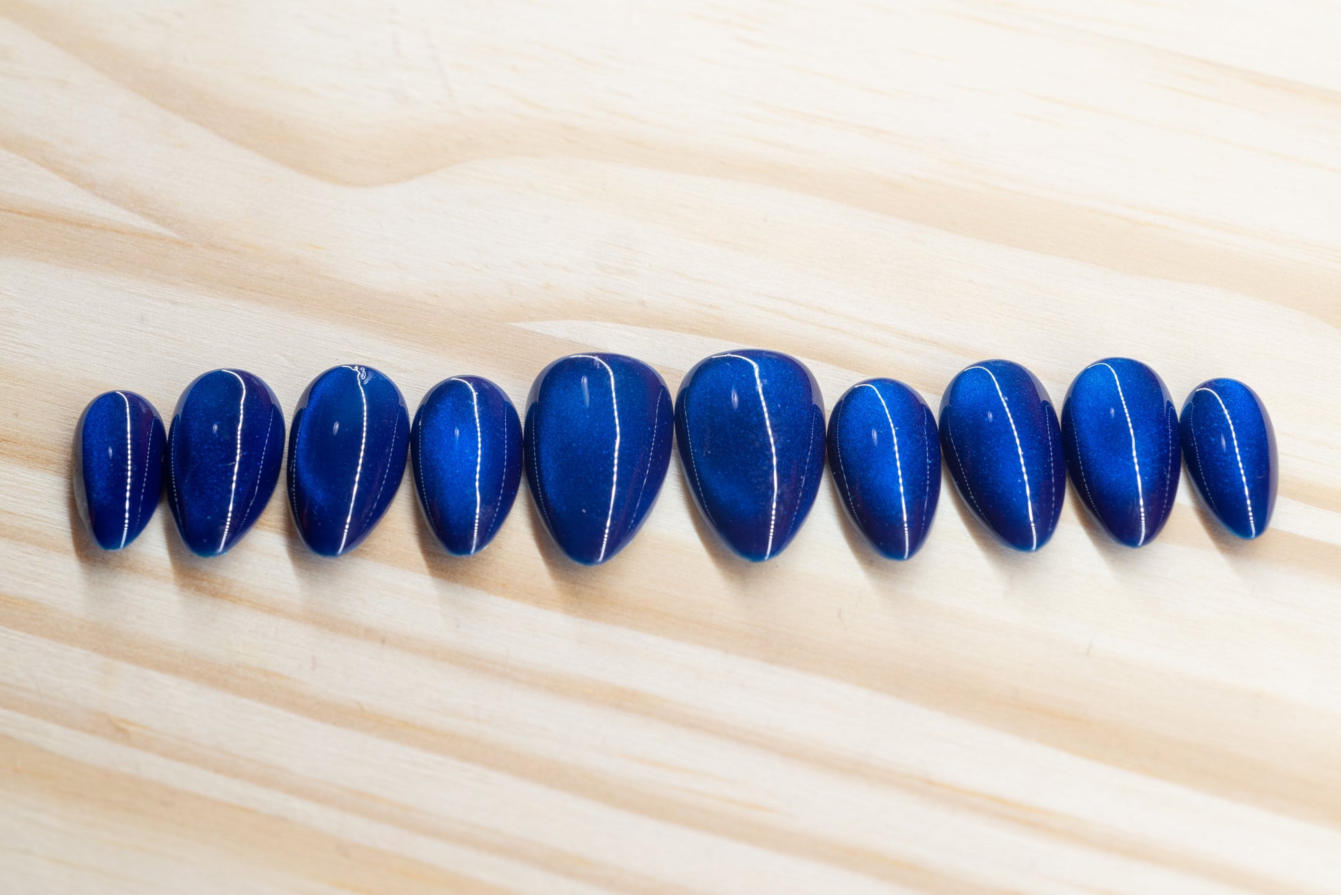 Deep blue cat eye effect press on nails featured on a wooden background